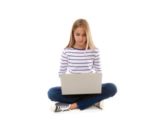 Naklejka premium Pretty young teen girl sitting on the floor with crossed legs and using laptop isolated