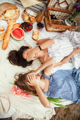 Beautiful young female friends lying on a blanket and close your eyes with your hands at a picnic on a summer day. The concept of leisure, privacy, communication, vacation, tourism