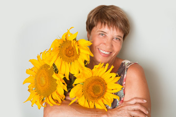 Naklejka premium Happy elderly woman with a sunflower on a gray background