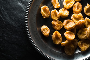 Dry dried apricots on a tin plate on a stone background closeup