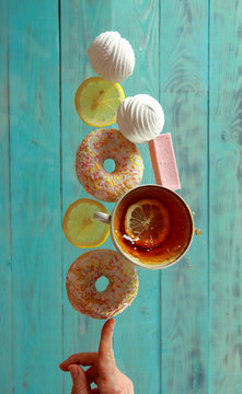 A Cup Of Tea, Marshmallows, Lemon, Candy And Donuts Balancing On His Finger