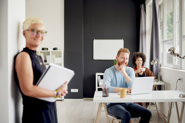 Senior standing in modern office against the wall and holding notebook 