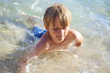 Young child boy having fun in the sea on the waves and enjoying water in summer holiday