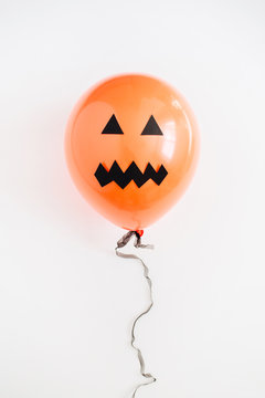 Halloween minimal concept. One orange balloon with scary face on white background. Flat lay, top view.