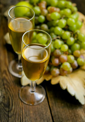 Two glasses and grapes in a decorative basket on a wooden surface.