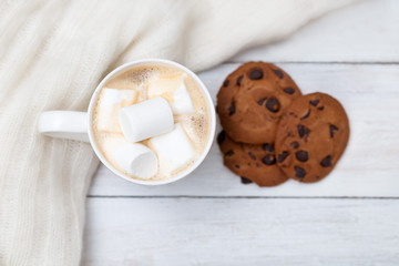 Cup of hot chocolate with marshmallows and a knitted sweater on a white wooden background
