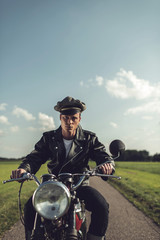 Vintage motorcyclist riding on country road in summer.