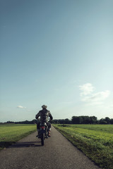 Rear view of motorcyclist riding vintage motorcycle on country road.