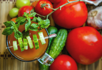 Tomato smoothies on a background of tomatoes and cucumbers.