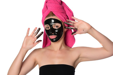 Beautiful female model with towel on her hear and black facial cosmetic mask on her face. Beauty cosmetic concept. Isolated on gray background.