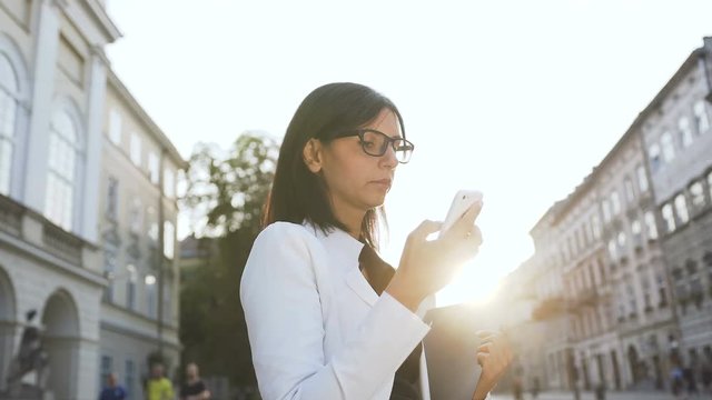 A young business woman wearing glasses in the morning goes to hte city and drops sms