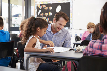 Obraz premium Teacher working with young schoolgirl at her desk in class
