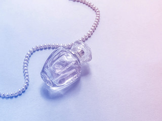 прозрачный флакон духов лежит на столе с бусами