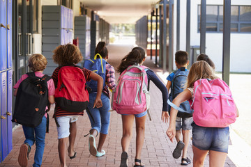 School kids running in elementary school hallway, back view