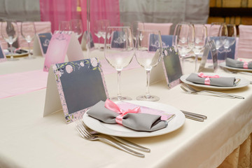 Rolled gray table napkin with pink ribbon and bar of chocolate with blank space for text on white empty plate. Table setting, free space. Table served for wedding banquet. Paper blank cards for guests