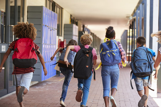 School kids running in elementary school hallway, back view