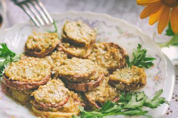 Rustic dinner with fried zucchini slices with nut sauce and greens. A white plate with food stands on a lacy rustic tablecloth, a bouquet with flowers in the background. Selective focus