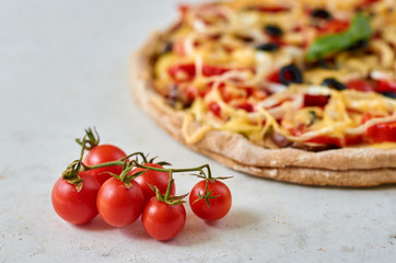 Hot vegetarian pizza with tomatoes, bell pepper, onion, black olives, cheese, spices on blurred white background close up decorated with fresh basil and small cherry tomatoes on foreground. Side view