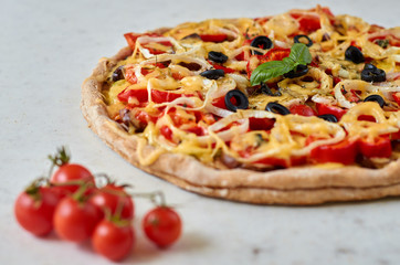 Hot vegetarian pizza with tomatoes, bell pepper, onion, black olives, cheese and spices on white background close up decorated with fresh basil and cherry tomatoes. Side view