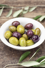 Purple and green olives  and olive branch on a wooden background.