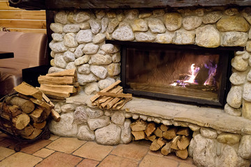 Stone fireplace with burning fire in country cottage. Flames of fire burning. Firewood against...