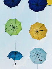 Interesting and colorful photo of bright and different-colored umbrellas just hanging above the boulevard with very light-blue sky at background.