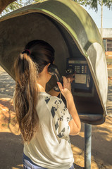 Girl standing, holding the phone, on her back, talking on the public phone