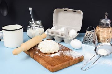 Fototapeta na wymiar Making homemade cookies. Raw dough, rolling pin, sieve, eggs, flour and icing sugar on blue table