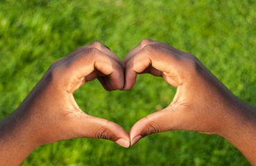 Black hands in heart shape with green grass background