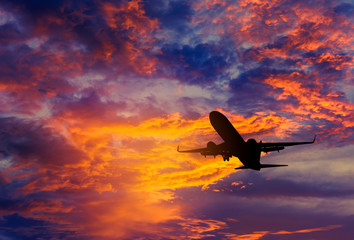   Silhouette passenger airplane flying away in to sky high altitude during sunset