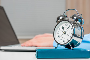 Alarm clock on desk in office close-up and secretary's hands out of focus