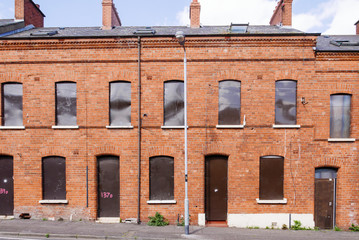 A long row of derelict houses in a street boarded up with steel plates.