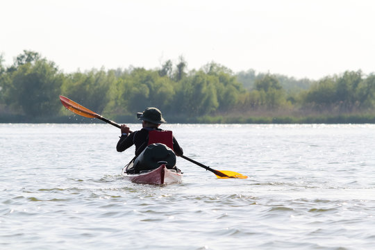 Man in red kayak in red life jacket kayaking in wild Danube river on biosphere reserve in spring