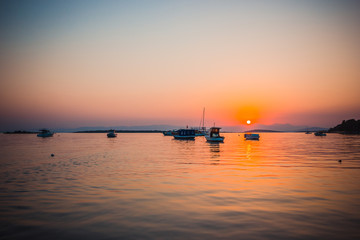 Naklejka premium Boats in the sea at sunset in summer with mountains on background