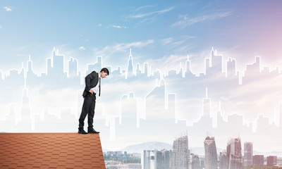 Businessman looking down from roof and modern cityscape at background. Mixed media