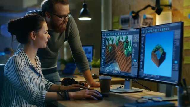 Female Game Developer Has Discussion with Male Project Manager While Working on a Game Level on Her Personal Computer with Two Displays. They Work in a Modern Loft Office Creative Environment. 