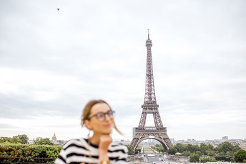 View on the Eiffel tower with young woman dreaming on the fourground during the cloudy weather in Paris. Woman is out of focus