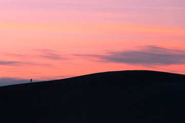 One sunset hiker walking sand dune crest