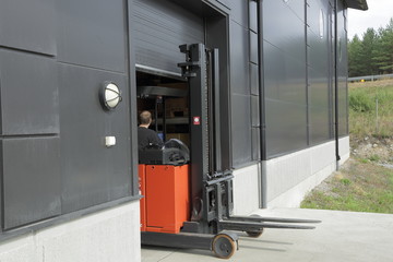 Picture of a industrial building. Male worker driving out of a warehouse on the fork-lift-truck