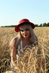Молодая светловолосая девушка в красной шляпе на пшеничном поле

