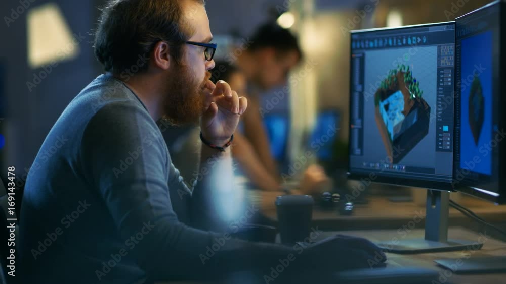 Poster Male Game Developer works on a Level Design on His Personal Computer with Two Displays. He Works for in a Creative Office Environment with Very Talented Colleagues. 4K UHD.