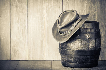 Wild West retro leather cowboy hat and old oak barrel. Vintage style sepia photo