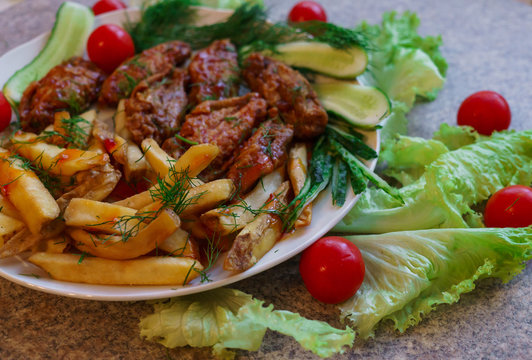 Chicken ribs in honey sauce with French fries and vegetables.