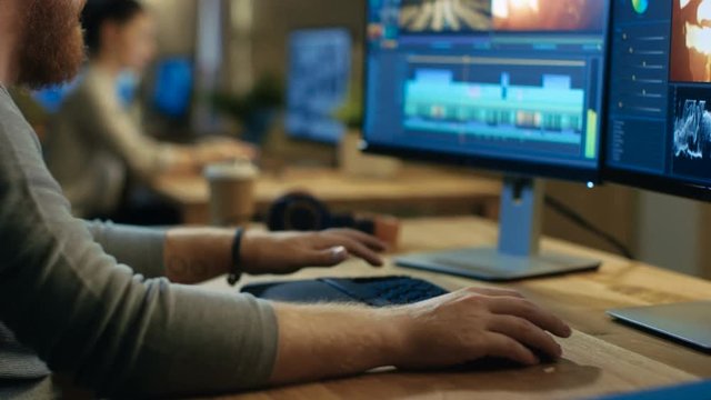 Male Videographer Edits and Cuts Footage and Sound on His Personal Computer with Two Displays. His Office is Modern and Creative Loft Studio. Shot on RED EPIC-W 8K Helium Cinema Camera.