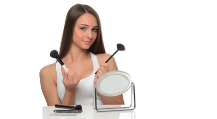  A young woman applying makeup on her face with a brush