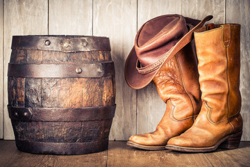 Wild West retro cowboy hat, old leather boots and aged oak barrel. Vintage style filtered photo