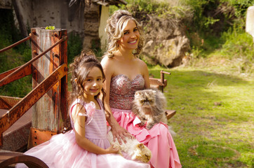 Beautiful woman and her cute little daughter looking at camera and smiling, wearing a princess dress, while they are hugging their cats, in outdoors