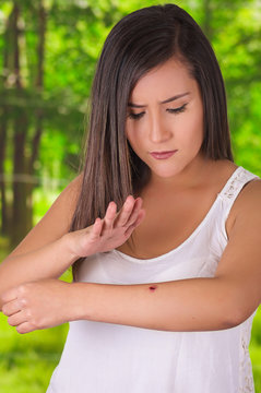 Young woman is using her hand to kill a mosquito over her arm, in a blurred green background
