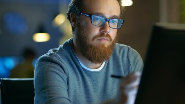 Talented Young Concept Artist Drawing on a Digital Pen Display Tablet While Sitting at His Working Place in Modern Loft Office. Late at Night. Shot on RED EPIC-W 8K Helium Cinema Camera.