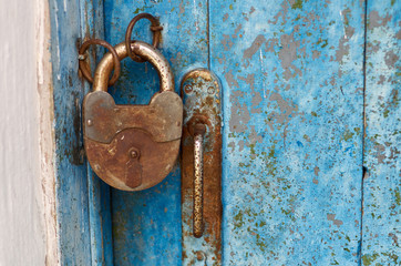 Old closed padlock rusty on wooden weathered door/An old wood blue painted door with metal rusted latch, padlock and antique door handle.Vintage lock